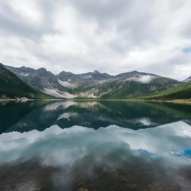 A serene mountain lake reflecting the surrounding peaks and cloudy sky.